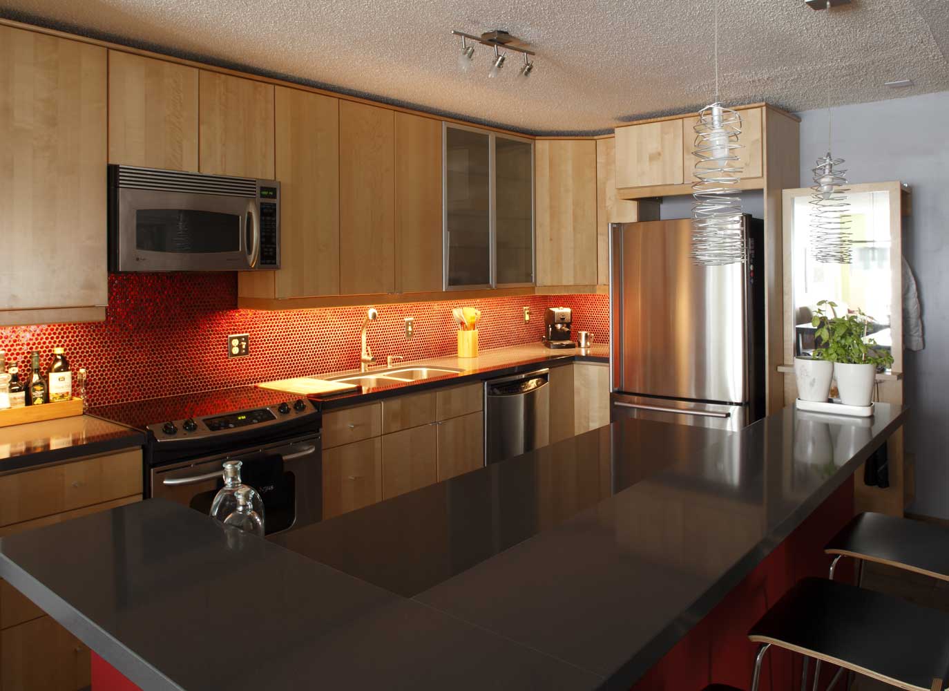 Kitchen with wood cabinetry, dark countertops and a red tile backsplash